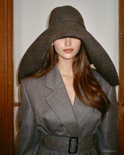 Nina Dobrev wearing gray coat against elegant drapery