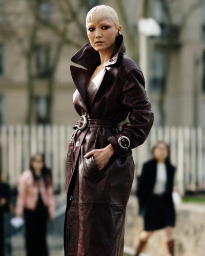 Pom Klementieff in glossy burgundy leather coat cinched at waist