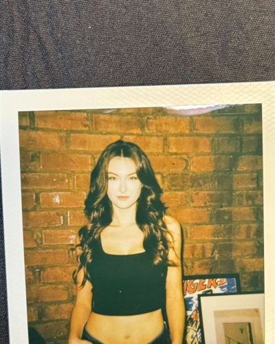 Rachel Pizzolato chic gray dress featuring sheer sleeves and red pillow