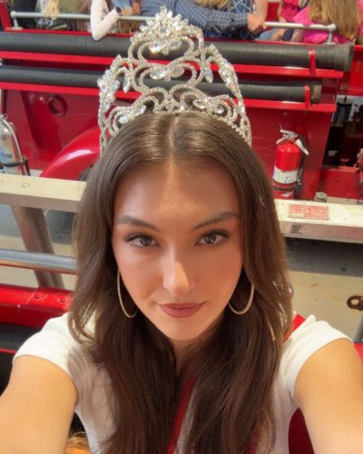 Rachel Pizzolato gray dress and black boots against lush greenery backdrop
