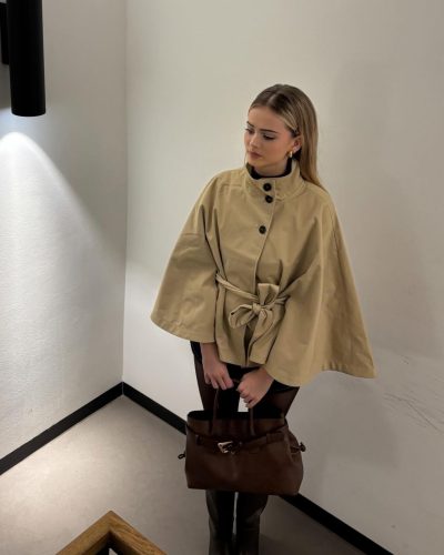 Sara Crumbleleg wearing fitted black top under beige trench coat.