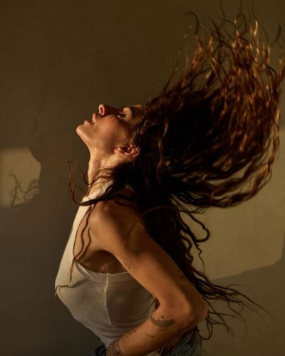 Sarah Shahi with flowing hair in white tank and blue jeans