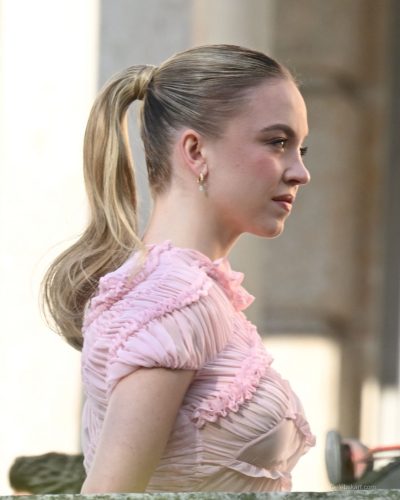 Sydney Sweeney pink dress with ruffles amidst vibrant natural scenery.