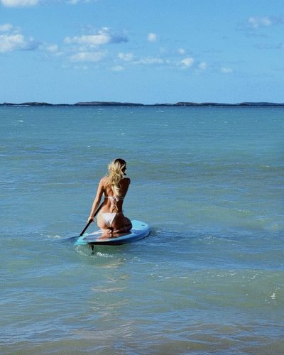 Sydney wearing teal bikini with minimal accessories by ocean.
